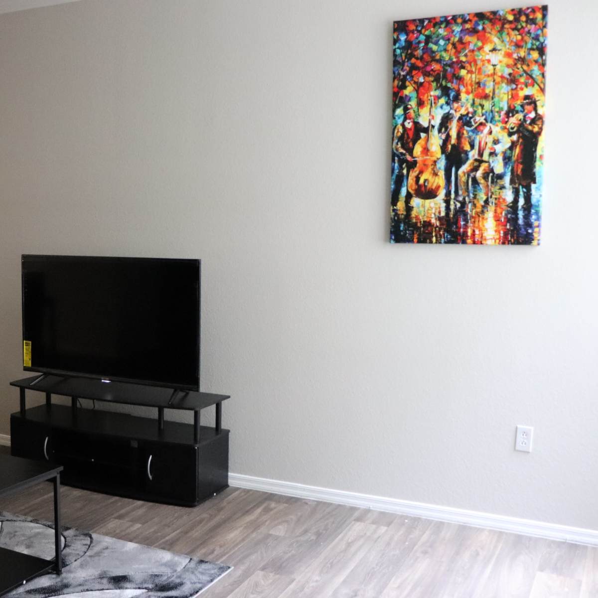 A living room with a television on a stand, a coffee table, and a colorful painting on the wall.