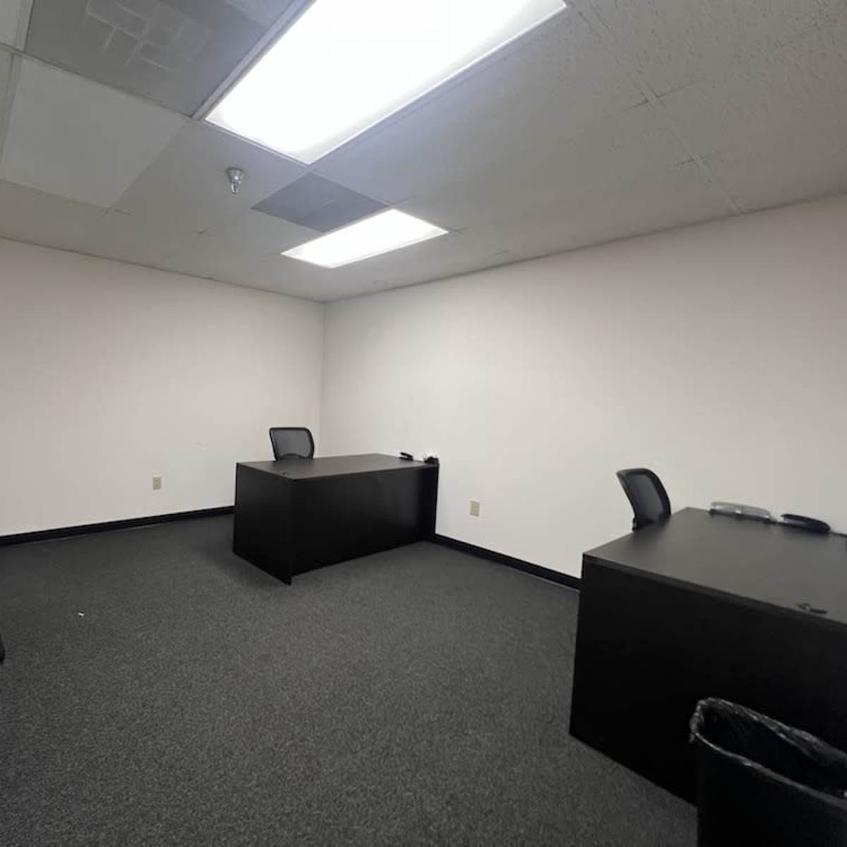 An empty office space featuring a desk, two chairs, and a window on one wall.