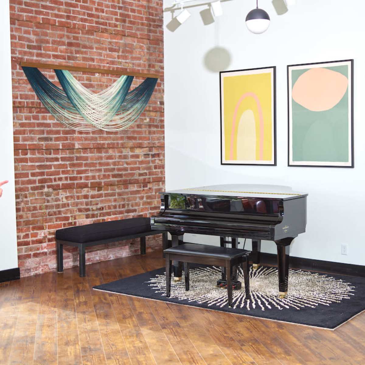 A black piano sits on a circular rug in a room with exposed brick walls and framed abstract art.