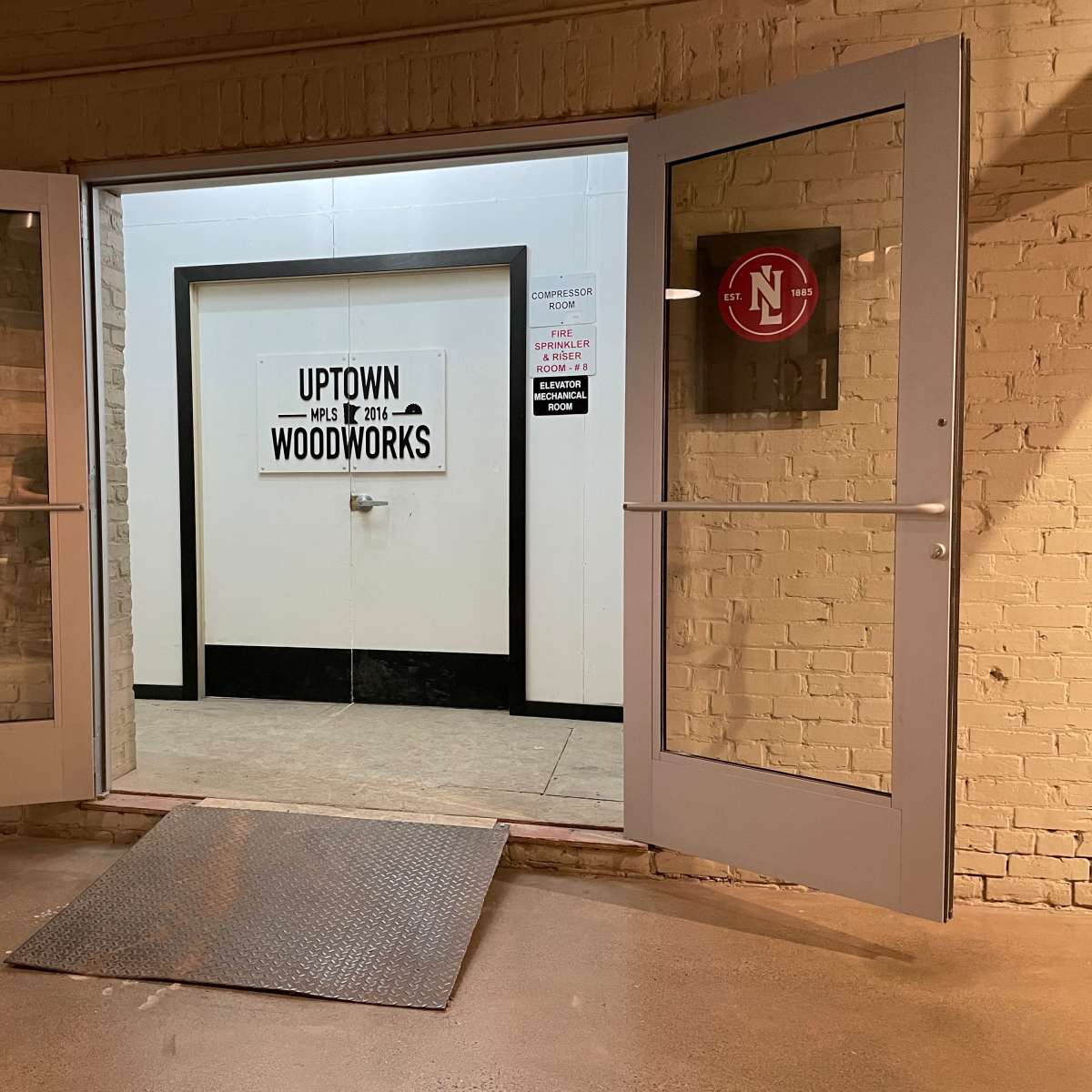 Double doors open to a hallway with a sign that says "UPTOWN WOODWORKS" on the wall opposite the entrance.