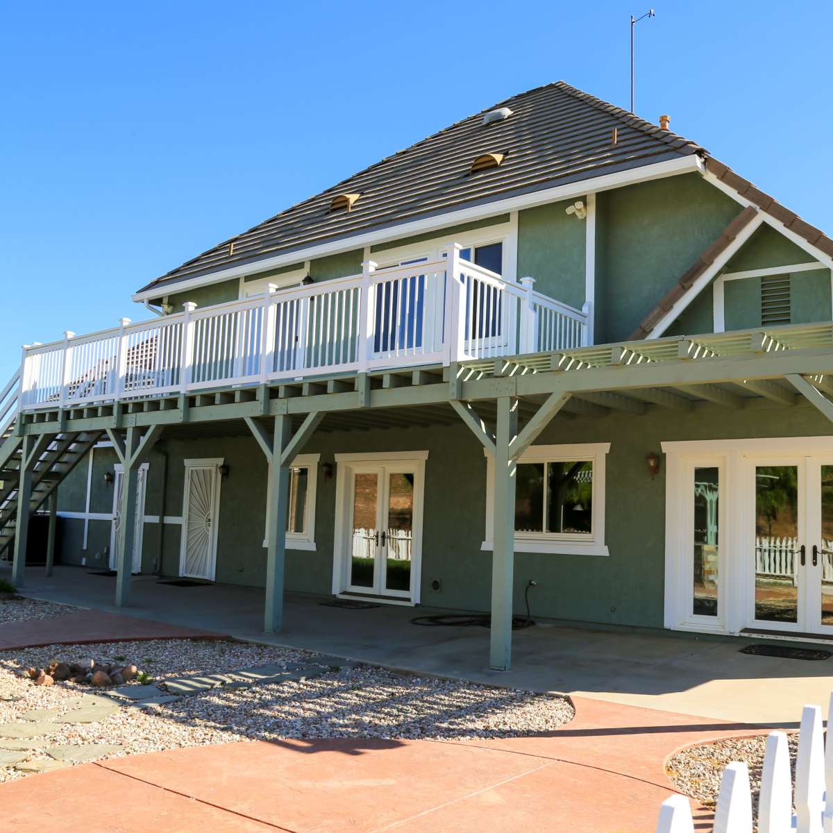 A two-story house with a balcony, surrounded by a patio and white picket fence.