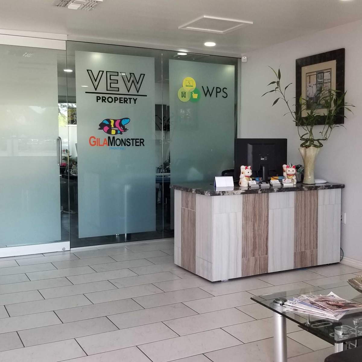 A modern office reception area with a glass wall featuring various logos and a sleek desk with decorations and informational materials.
