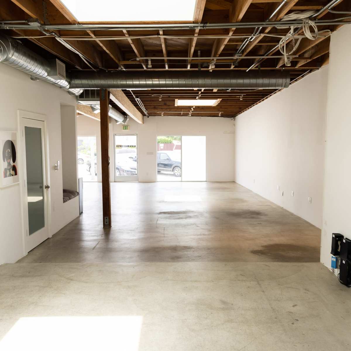 An empty, minimalistic interior space with concrete flooring and exposed wooden beam ceilings.