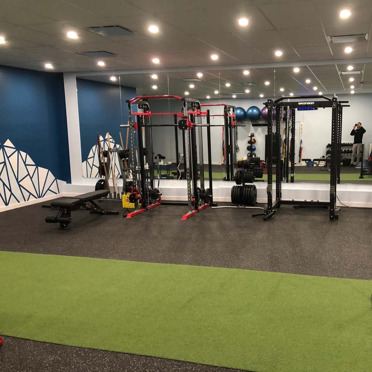 The gym features workout equipment including free weights, a bench, and a treadmill on a green turf floor.