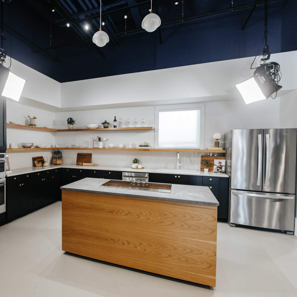 A modern kitchen features black cabinets, a large wooden island with a stone countertop, and stainless steel appliances.