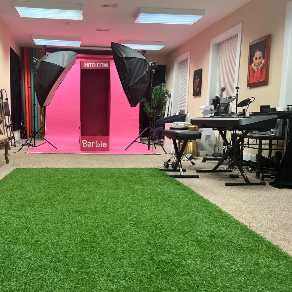 A room with a bright pink backdrop labeled "LIMITED EDITION" flanked by two professional lighting setups, while an artificial grass carpet covers the floor.