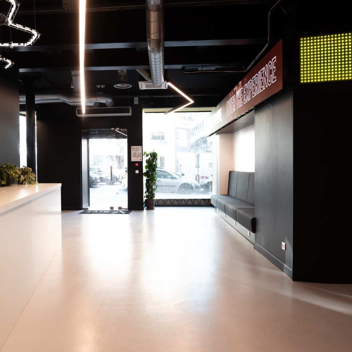 A modern reception area featuring a sleek white counter, black seating along the wall, and bright signage overhead.