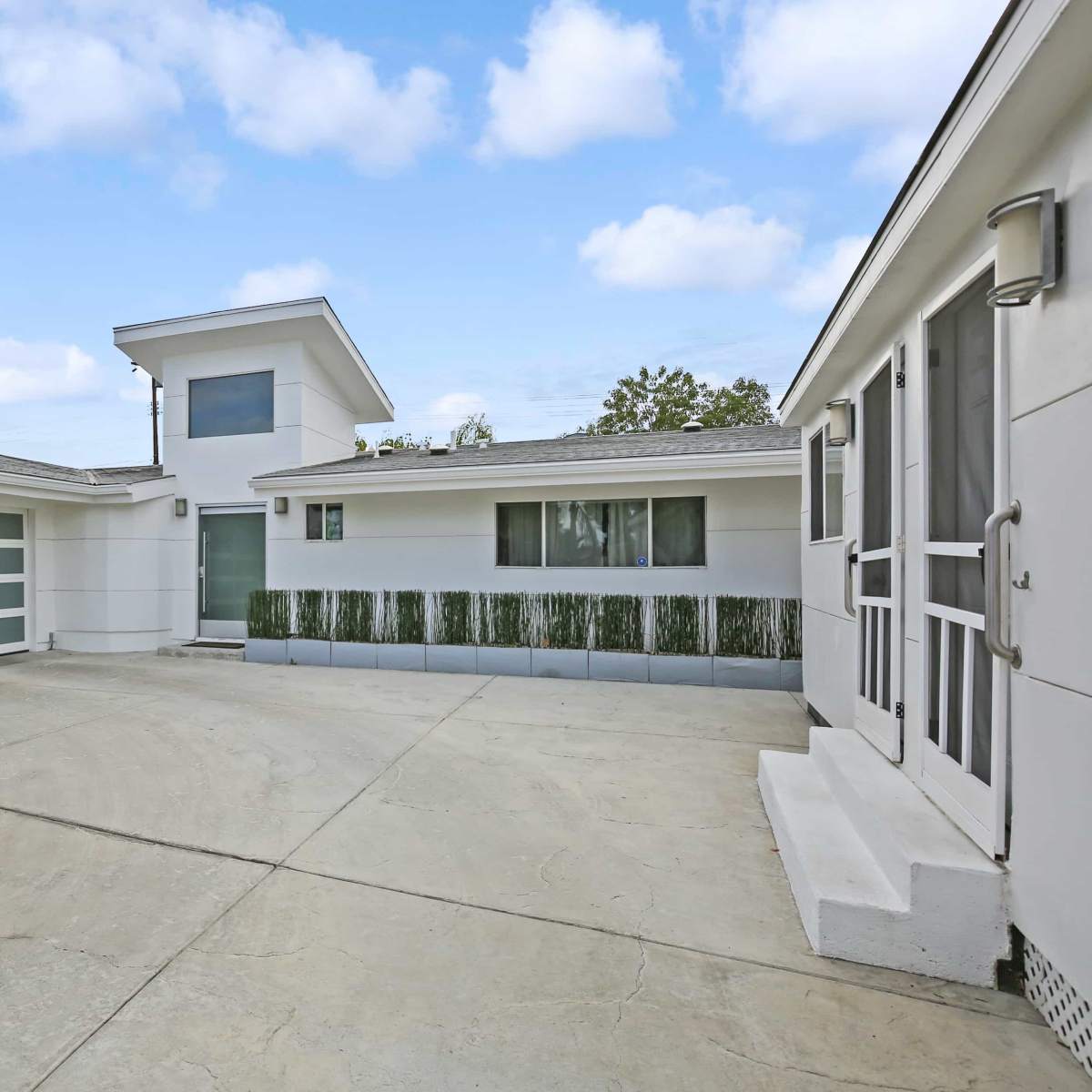 A modern house with a paved driveway, large garage door, and landscaped greenery surrounding the structure.