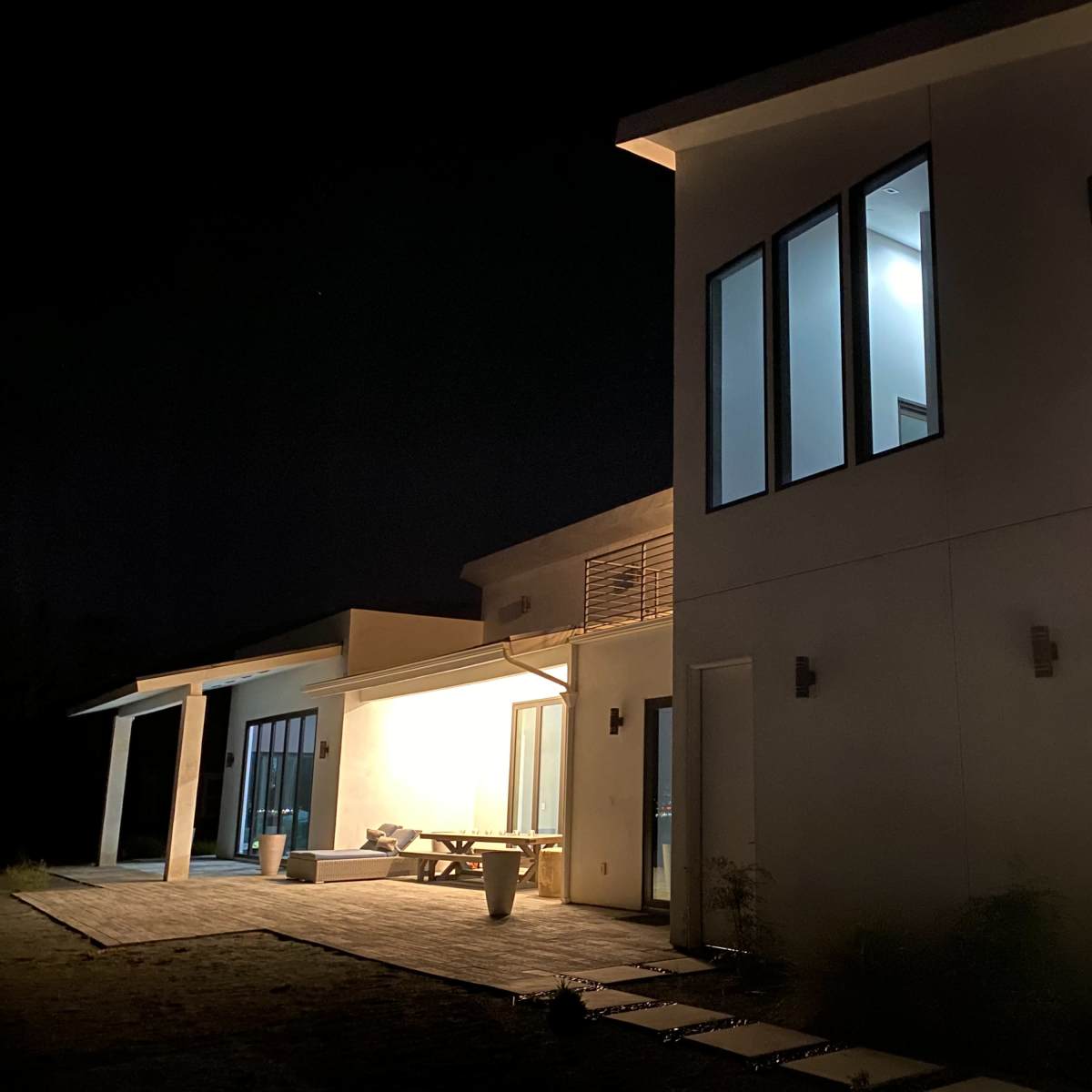 A modern house is illuminated at night, showcasing large windows and a patio area.