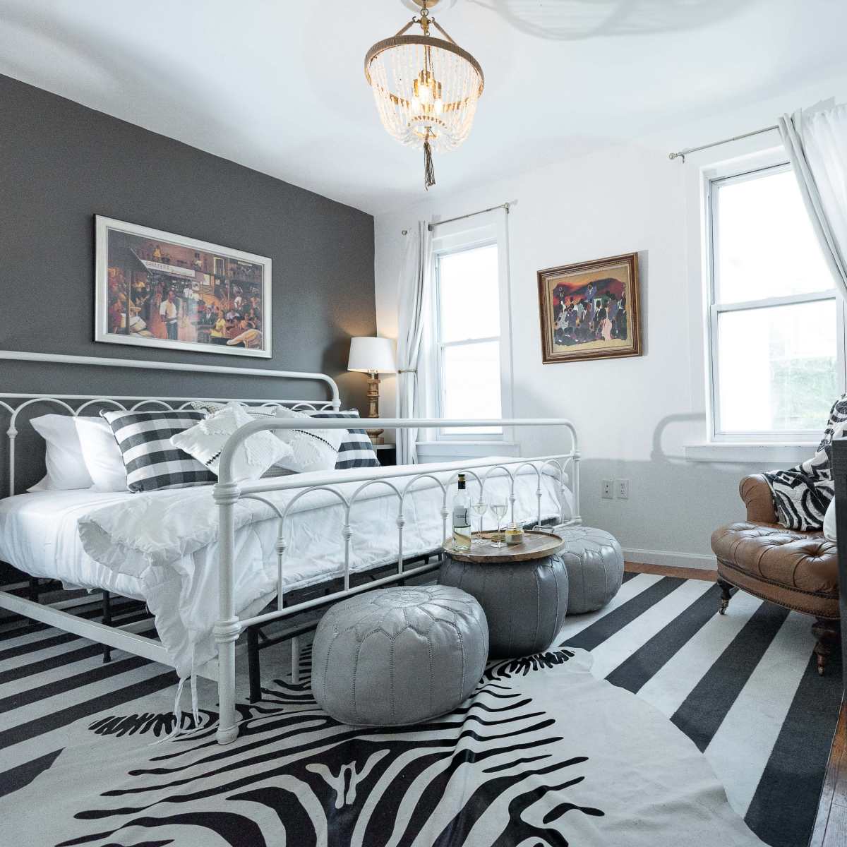 The bedroom features a white metal bed with black and white bedding, a leather armchair, and a striped rug.