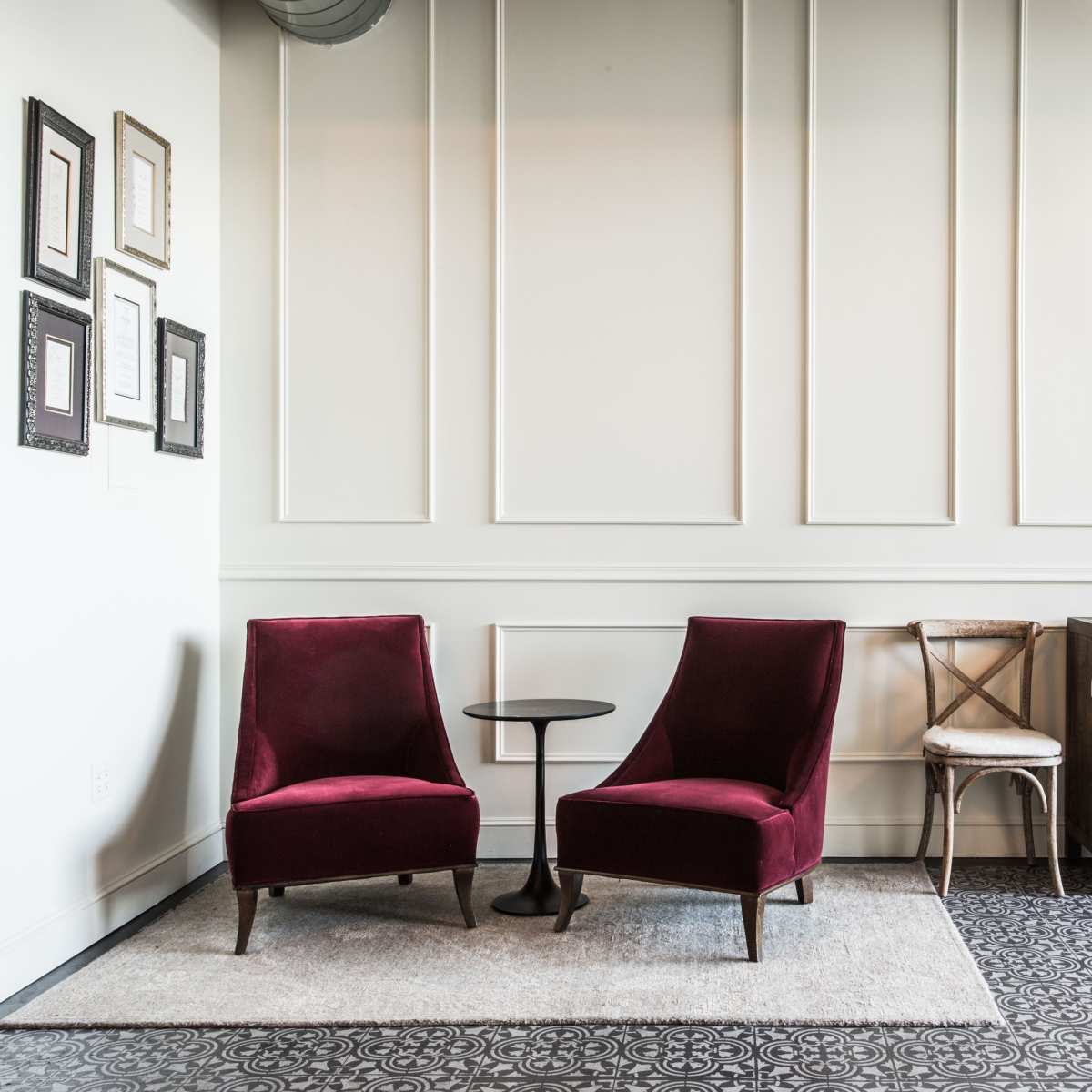 A corner of a room features two red chairs with a small black table between them, set against a wall with decorative frames and a cabinet nearby.