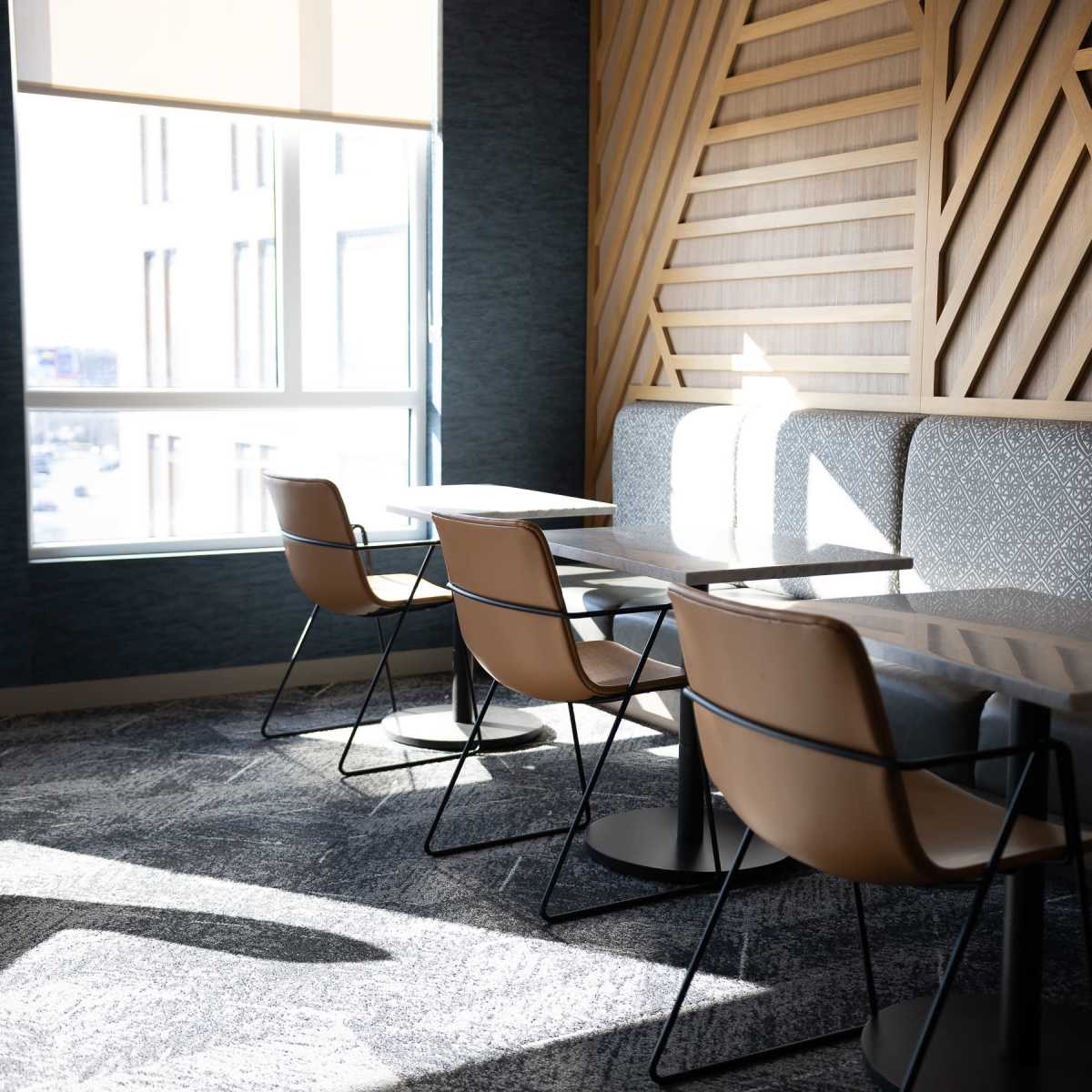 A well-lit seating area with wooden paneling, featuring two tables and four chairs against a window.