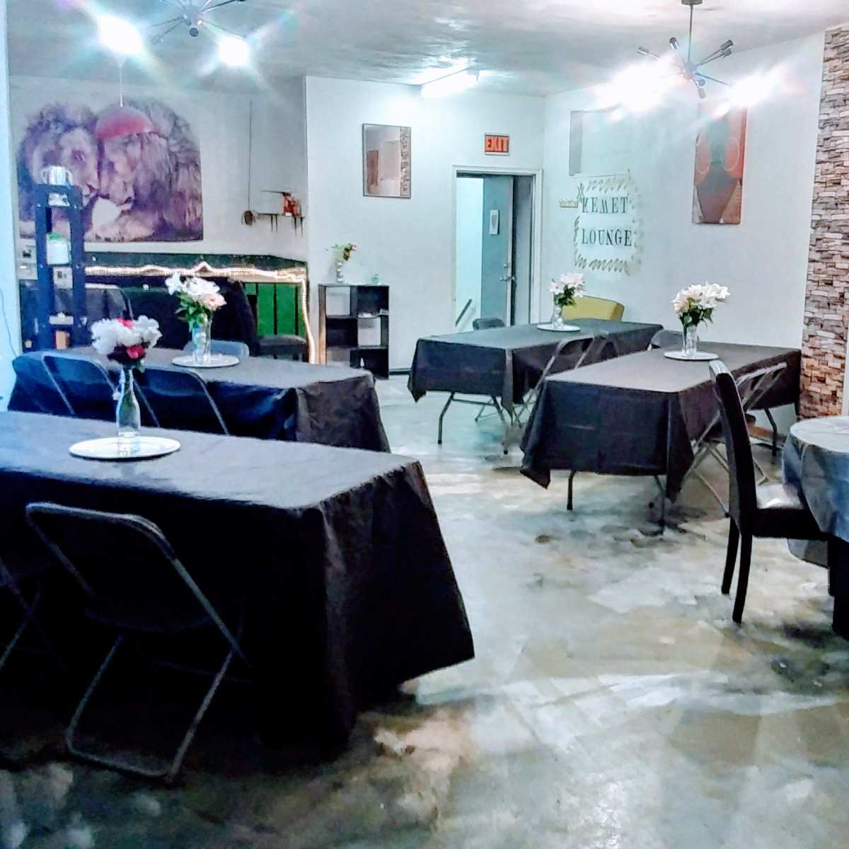 A dining area with several tables covered in gray tablecloths, arranged in a spacious room with simple decor and flowers on each table.