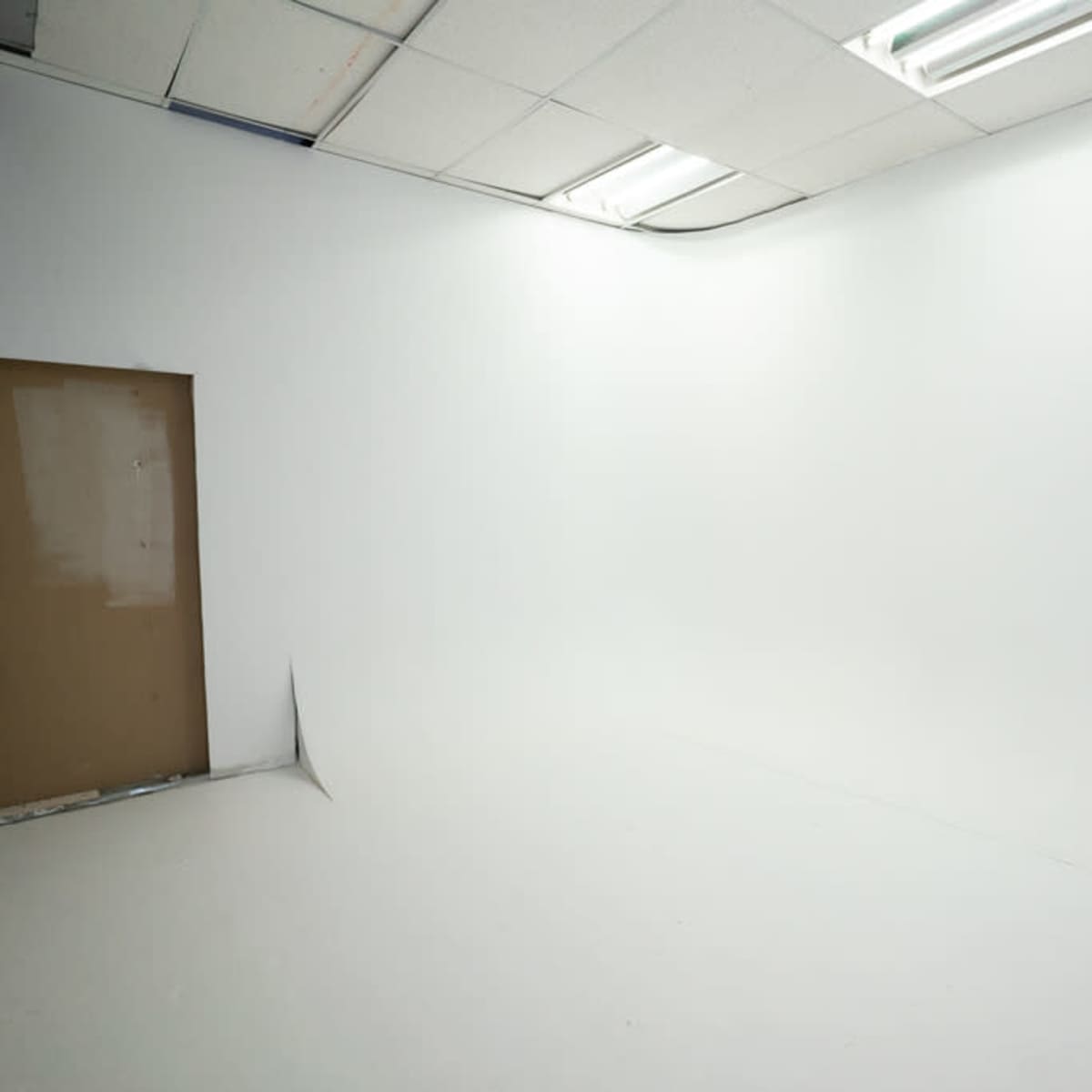 A spacious white room with a flat, empty floor and a single brown door.