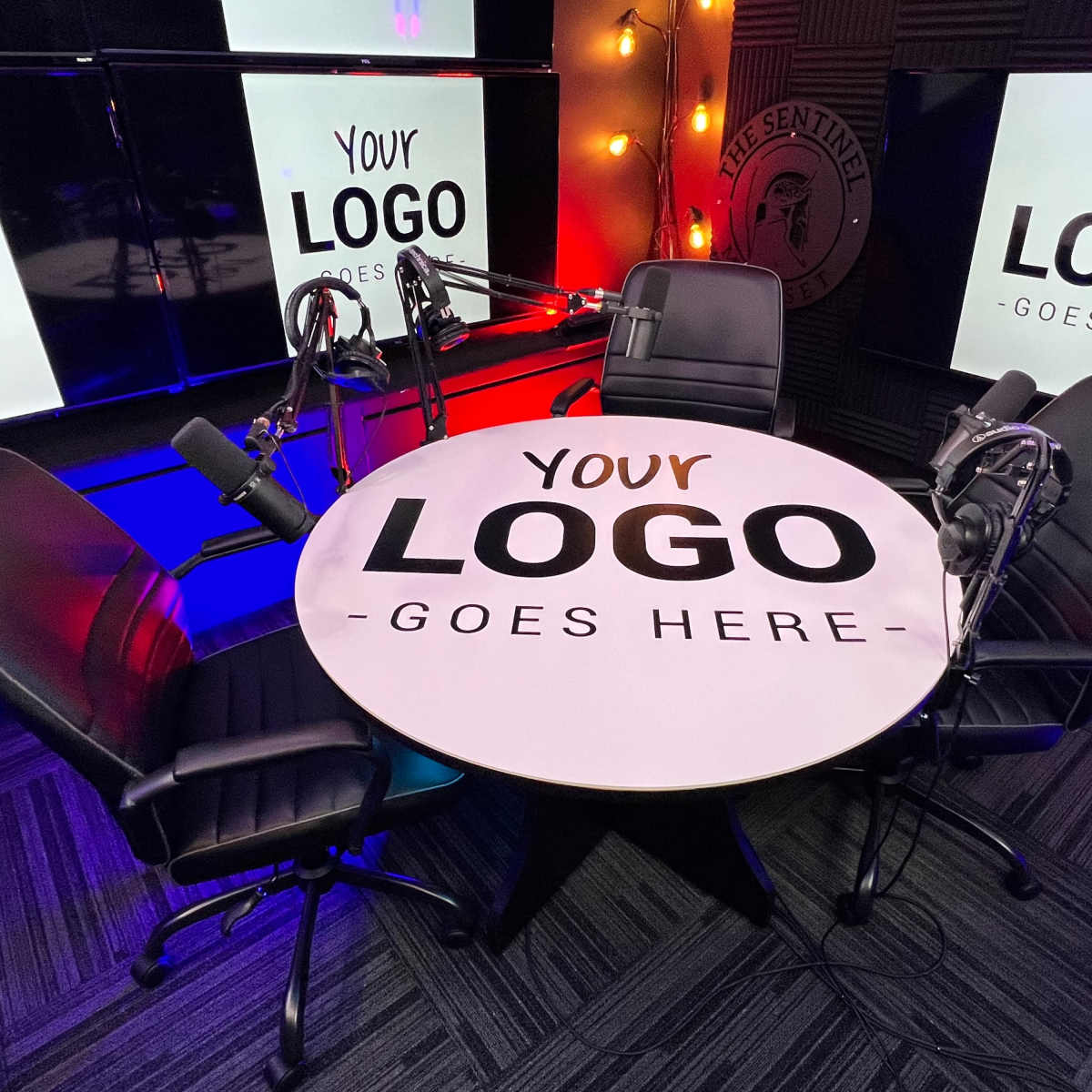 A round table with microphones and three black chairs is set up in a studio labeled "Your Logo Goes Here."