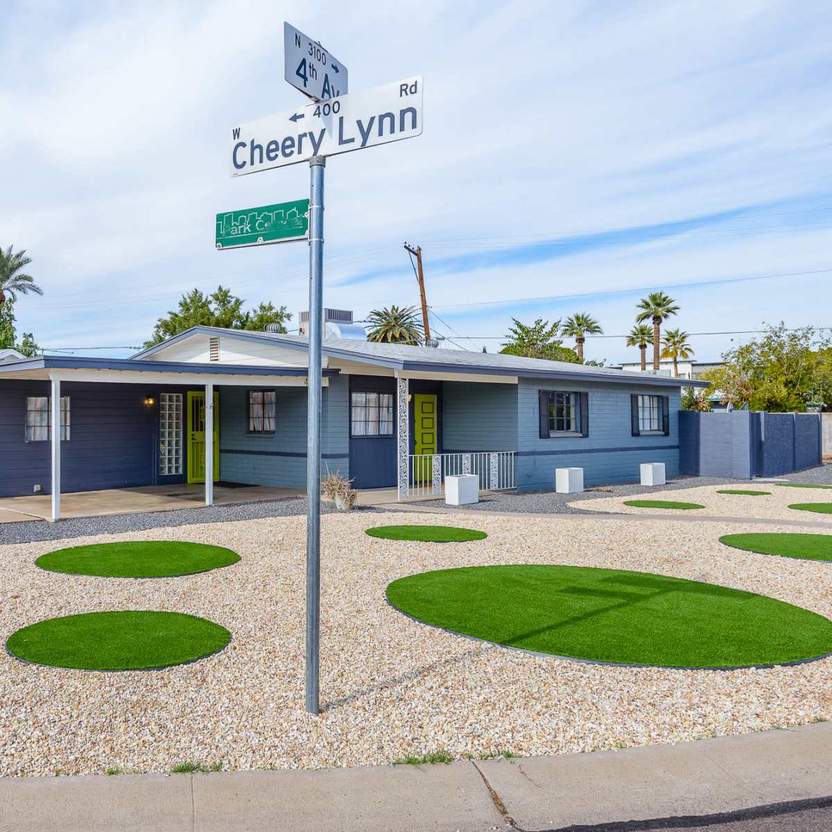 A blue house with a landscaped yard featuring circular patches of green grass and a sign for Cheery Lynn Road at the corner.