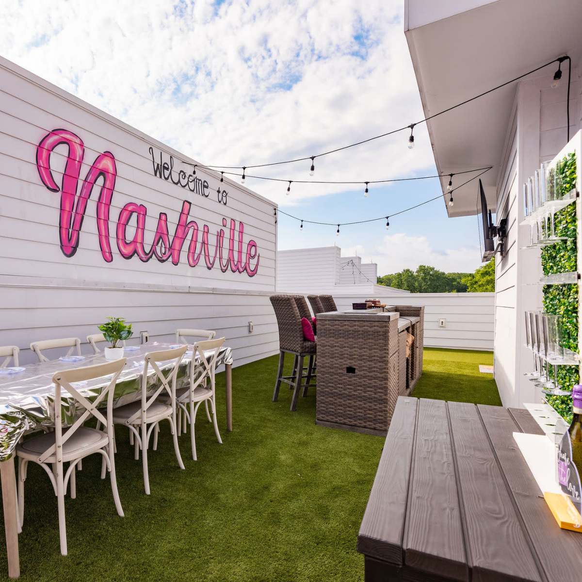 A rooftop terrace in Nashville featuring white walls, string lights, a long dining table, and wicker furniture.