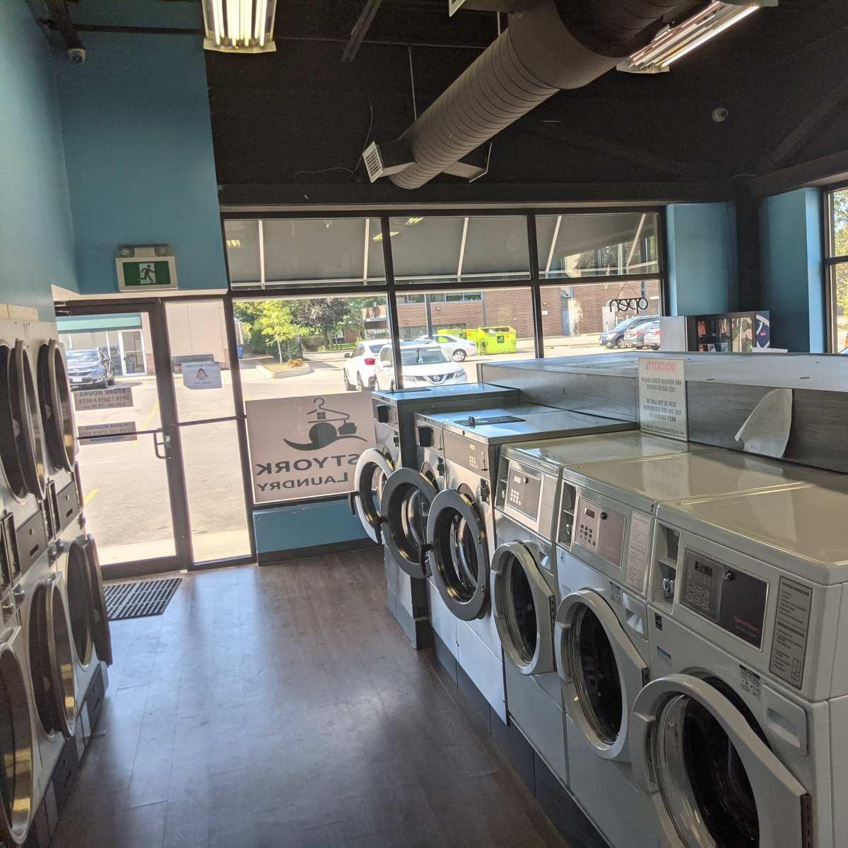 A laundromat with rows of washing machines and a glimpse of the outside through large windows.