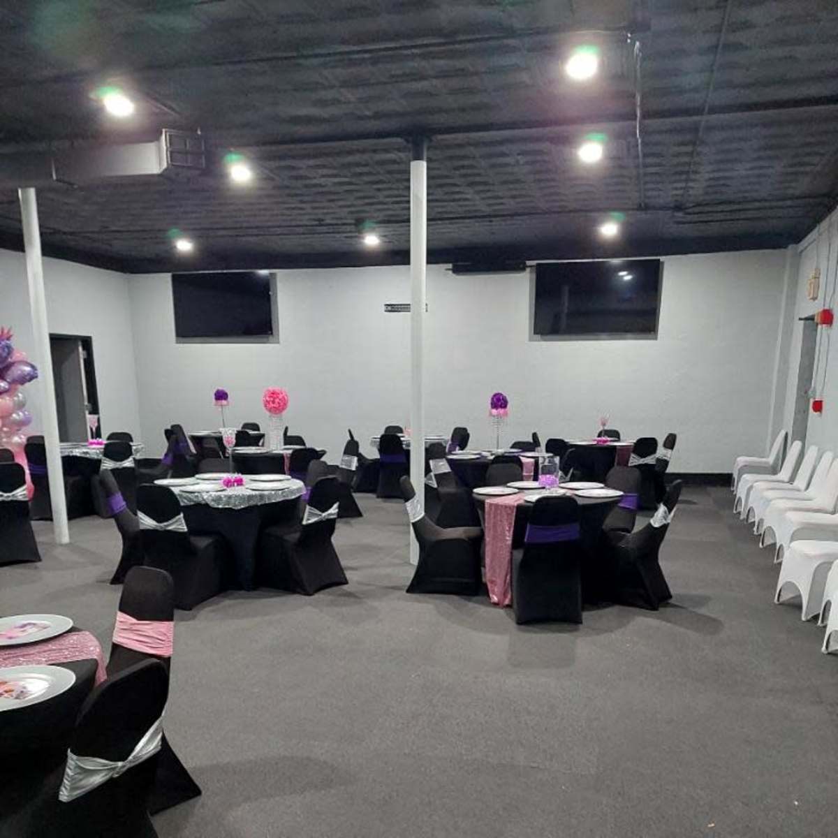 A party venue with several round tables set with black and pink decorations, surrounded by black and white chairs.
