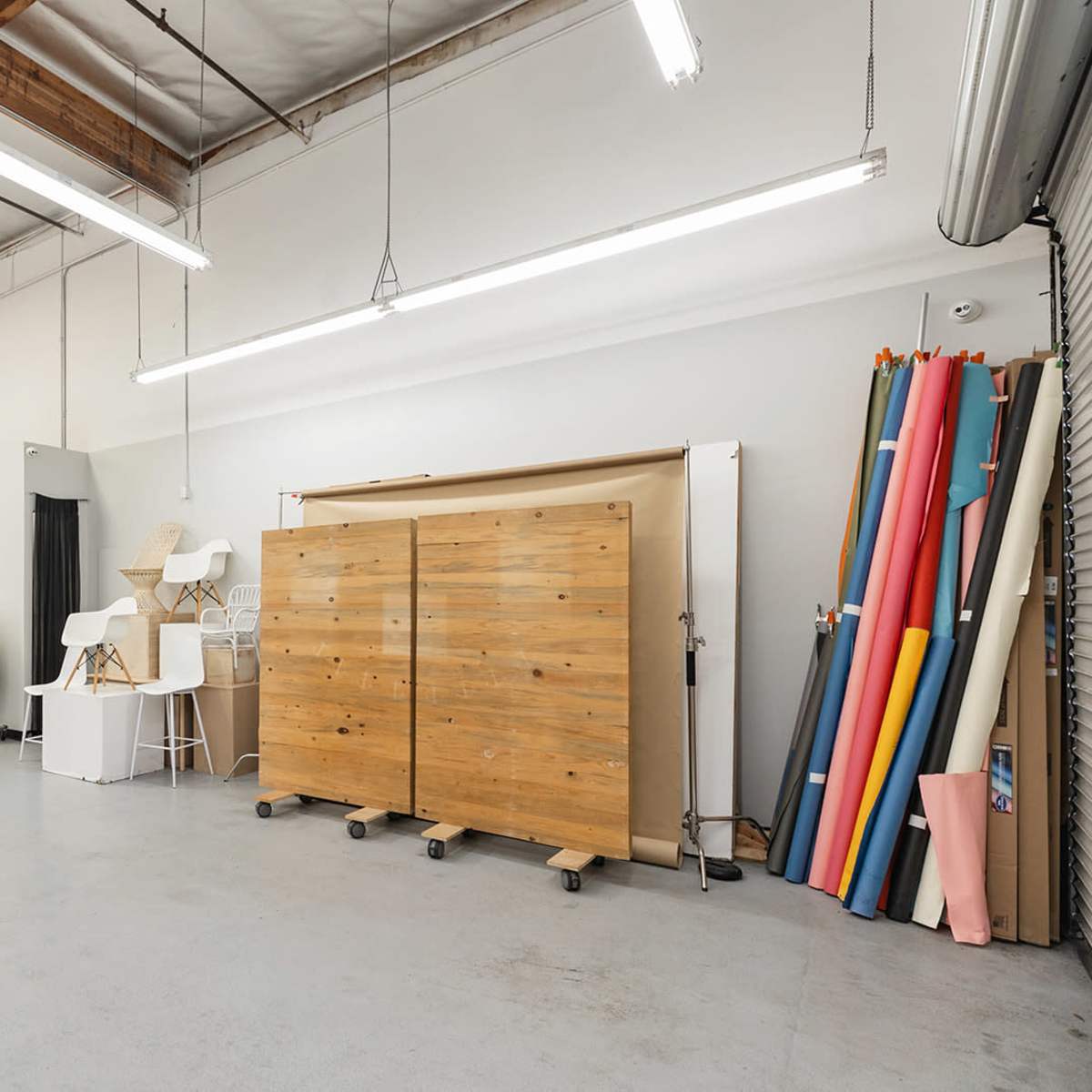 A spacious studio with a wooden storage unit on wheels and a collection of colored paper rolls against the wall.