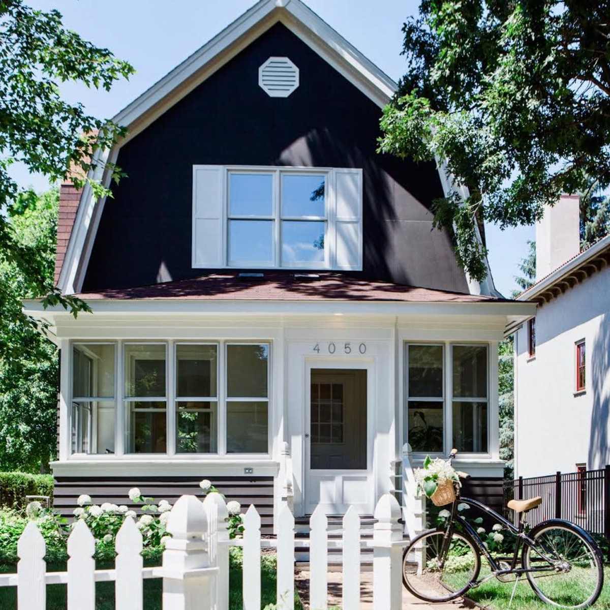 A black-painted house with white trim features a picket fence and a bicycle parked alongside a stone pathway.