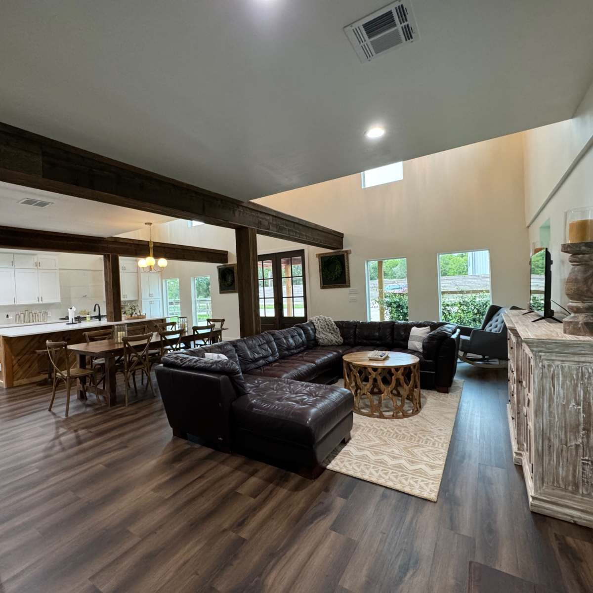 A spacious living area with a dark leather sectional sofa, a wooden dining table, and large windows that provide natural light.