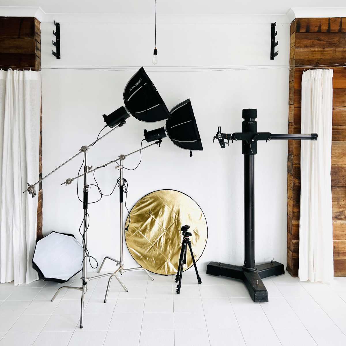 A photography studio setup with two light stands, a gold reflector, and a tripod against a white wall.