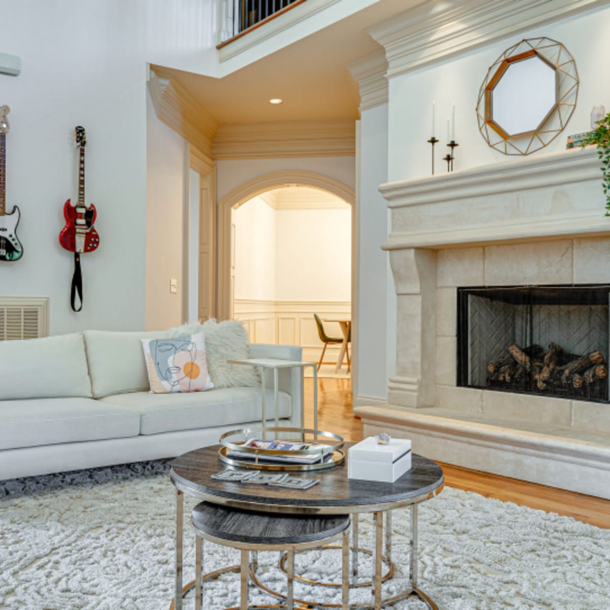 A living room featuring a white sofa, a stone fireplace, two coffee tables, and guitars hanging on the wall.