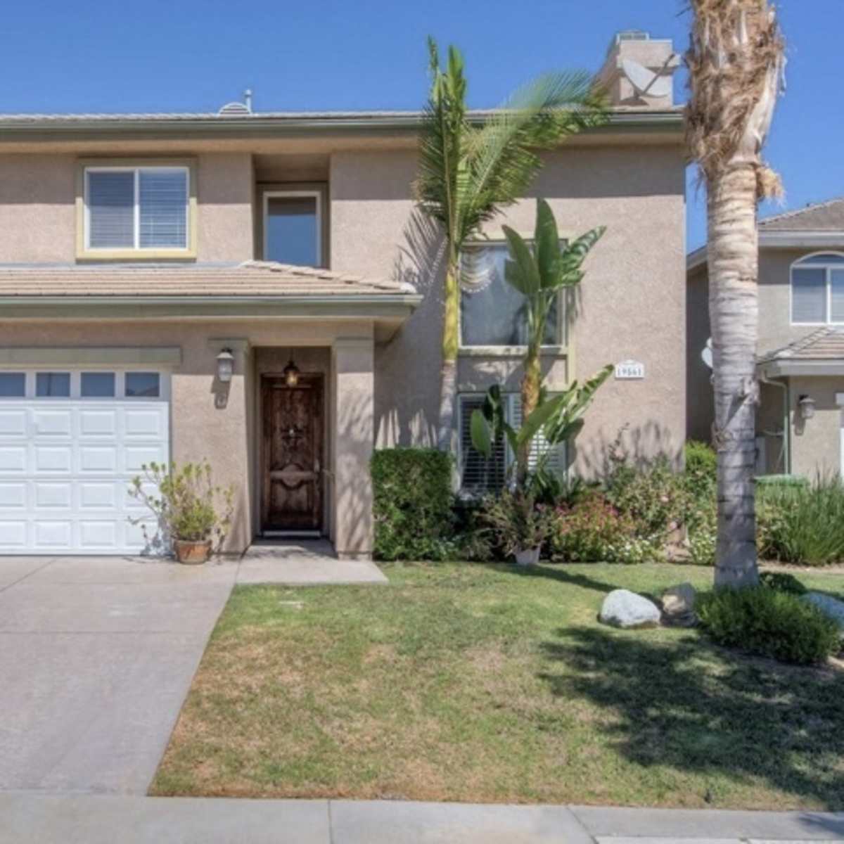 A two-story house with a garage and front yard, featuring a paved driveway and landscaping.
