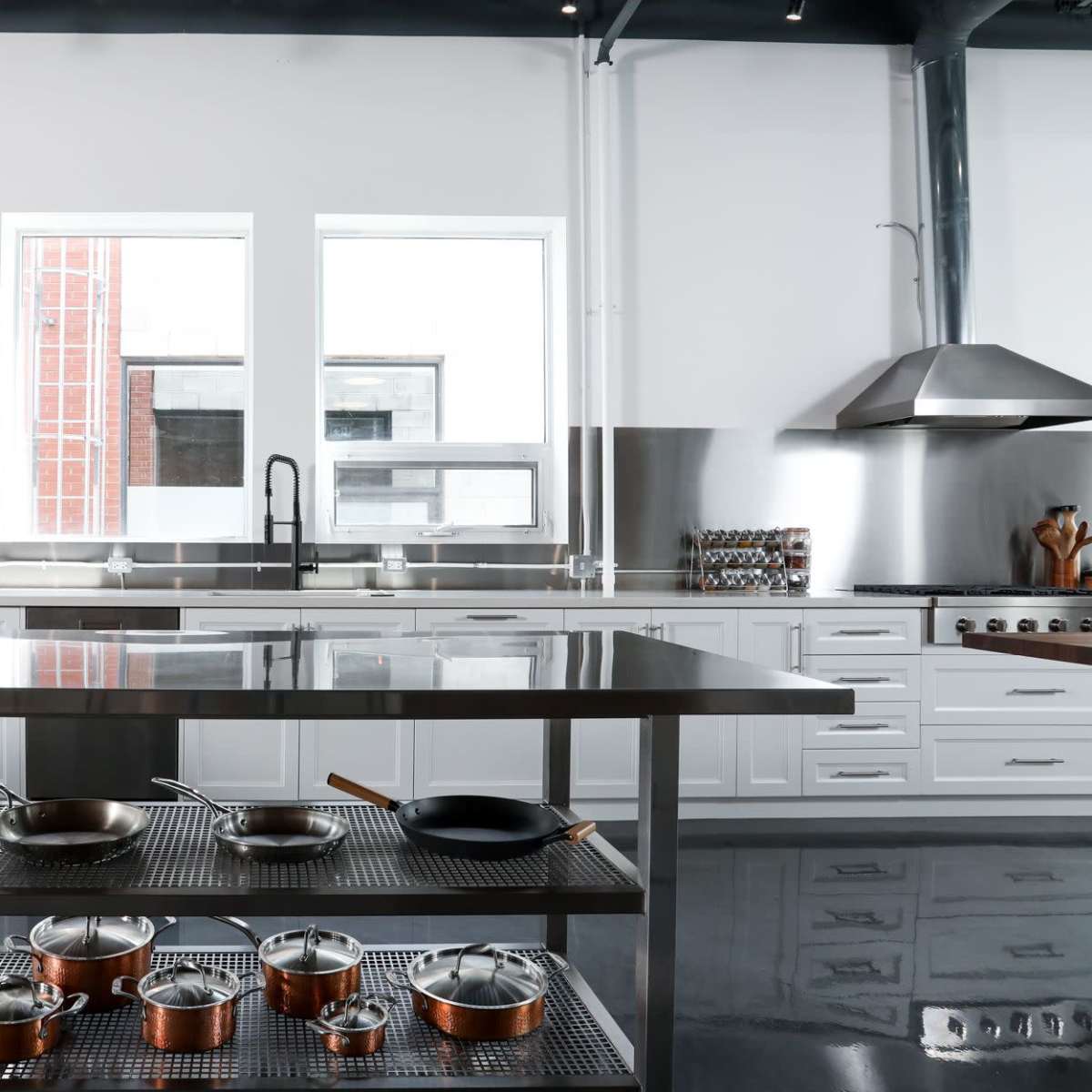 A modern kitchen with stainless steel appliances, a central island with a metal frame, and various cooking pots arranged on open shelves.