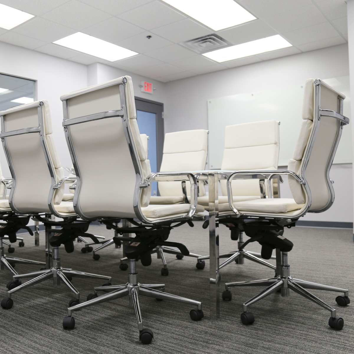 A row of eight white office chairs on wheels is positioned around a meeting room table in a modern workspace.