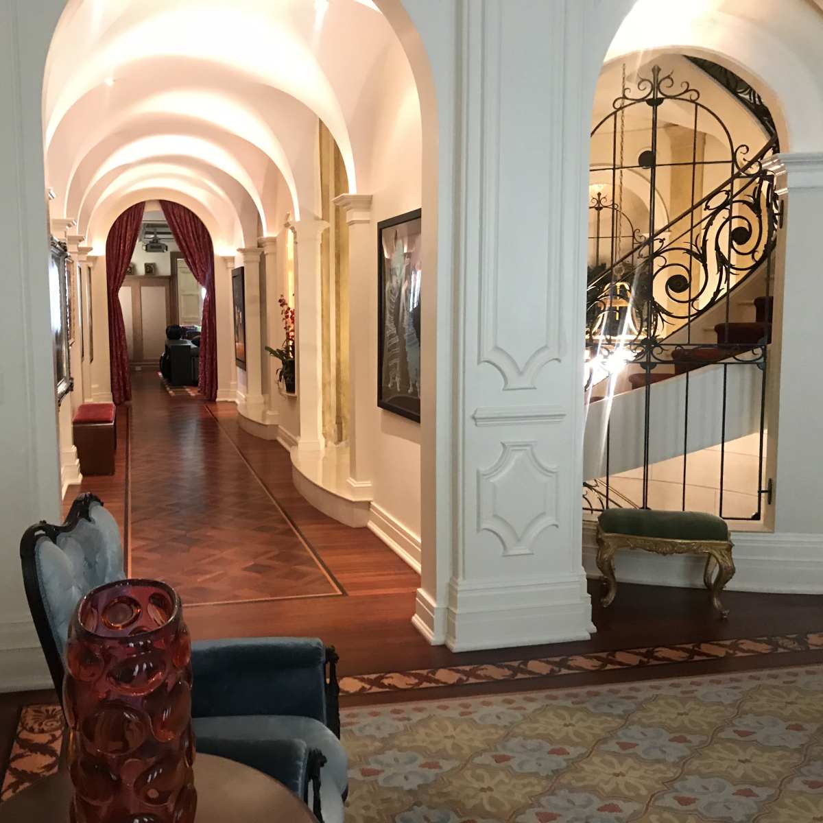 A long hallway with arched ceilings, decorative wall moldings, and wooden flooring, leading to a staircase.
