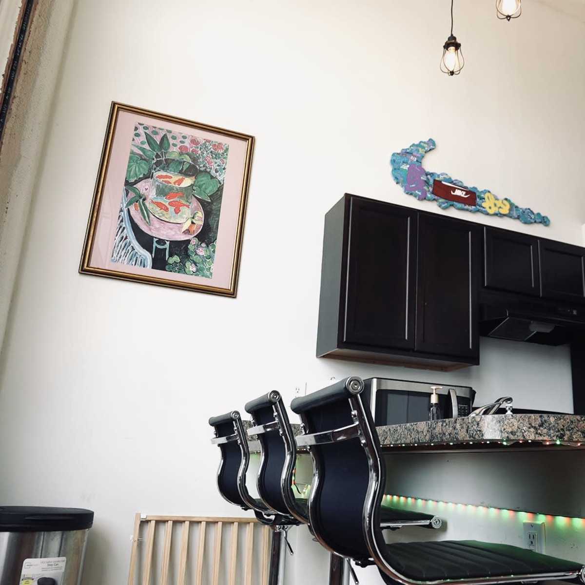 A modern kitchen area with dark cabinets, a granite countertop, and colorful artwork on the wall.