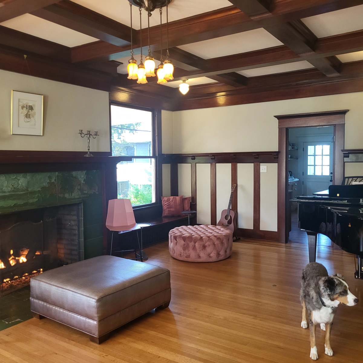 The living room features a fireplace, seating areas, a grand piano, and a dog standing on the hardwood floor.