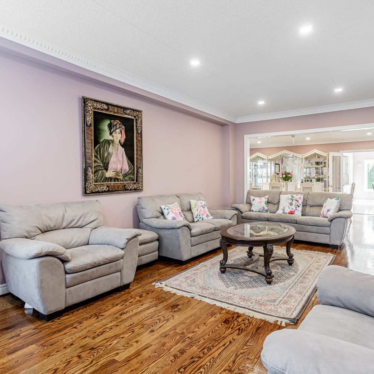 The living room features light gray sofas arranged around a round wooden coffee table on a decorative rug, with a framed portrait hanging on the wall.