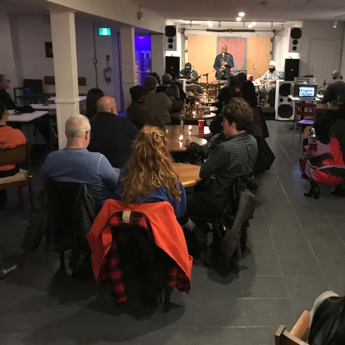 A group of people is seated at tables watching a live musical performance in a small venue.