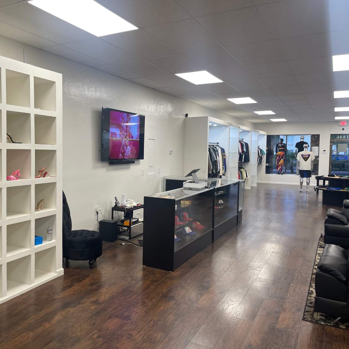 A retail clothing store interior featuring a shelving unit, a display television, and various items of clothing arranged along the walls.