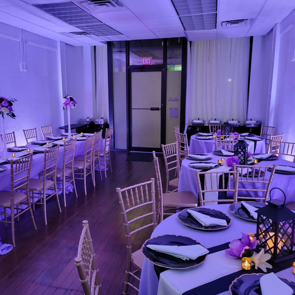 A beautifully arranged banquet hall with several tables set for dining, featuring purple and black tablecloths, candles, and floral centerpieces.