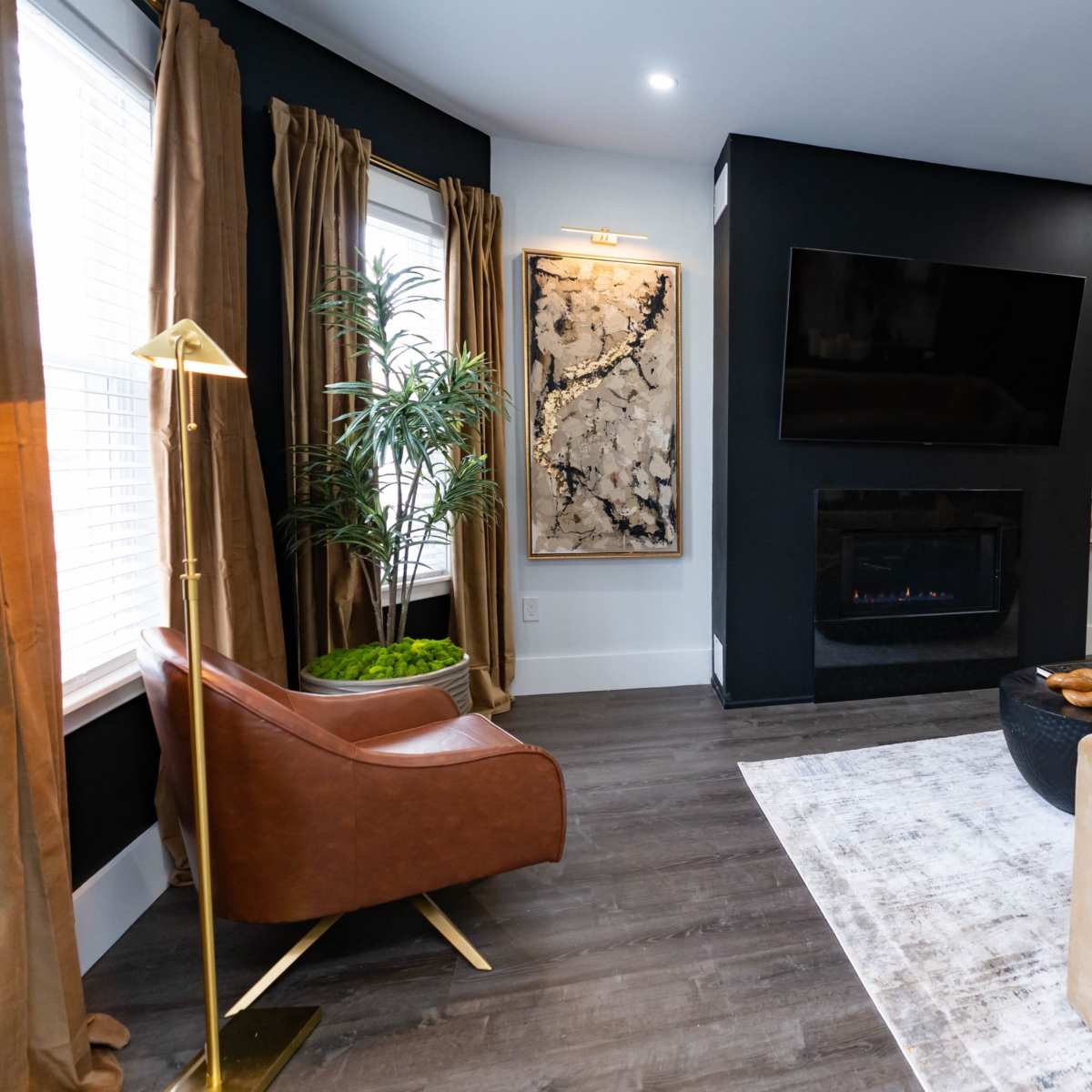 The living room features a modern seating arrangement with a plush sofa, an accent chair, and a wall-mounted television, complemented by a fireplace and decorative artwork.