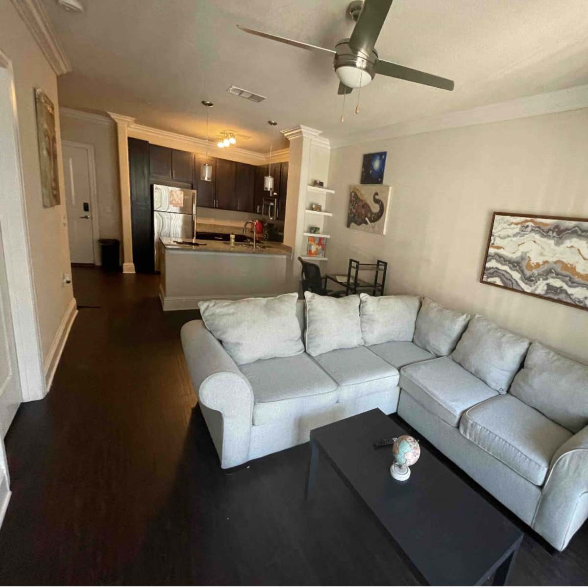 A living room with a light gray sectional sofa, a black coffee table, and an open kitchen in the background.