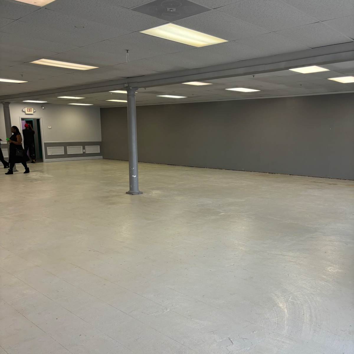 A spacious, empty room with a gray-painted wall, a central support column, and overhead fluorescent lighting.