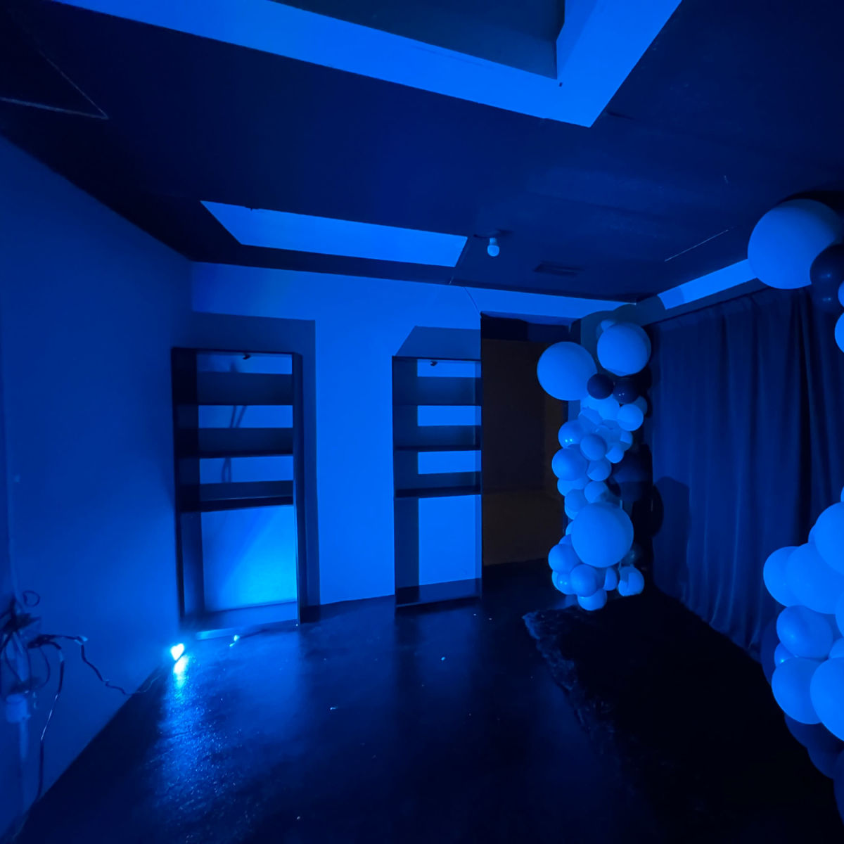 A dimly lit room with blue walls and decorations featuring clusters of white and dark balloons against a blue backdrop.