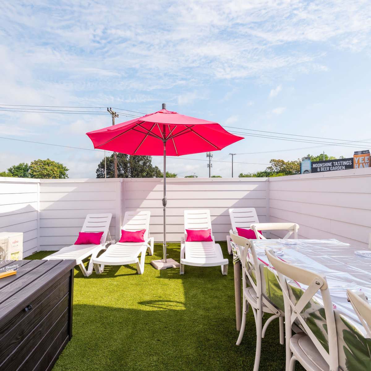 A rooftop patio with white furniture, green grass, a large red umbrella, and a table set for dining.