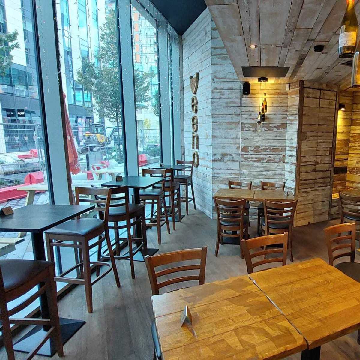 The interior of a restaurant featuring wooden tables and chairs, with large windows allowing natural light to illuminate the space.