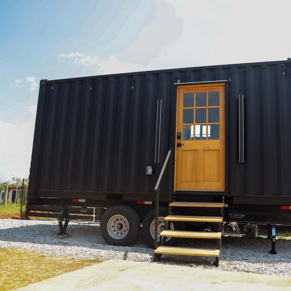 A black shipping container converted into a portable structure with a wooden door and steps leading up to it.