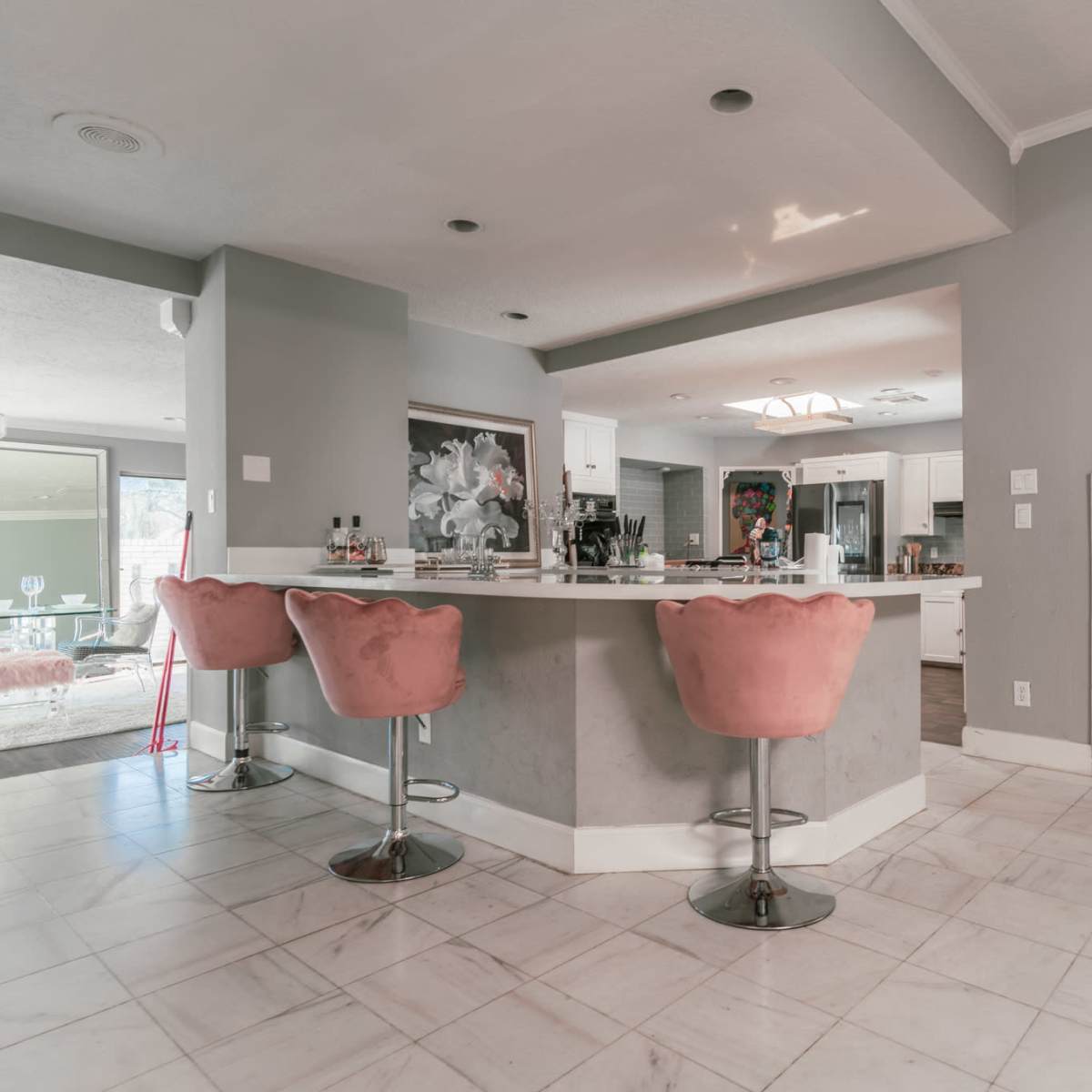A modern kitchen features a marble fireplace, a large island with pink bar stools, and contemporary decor.