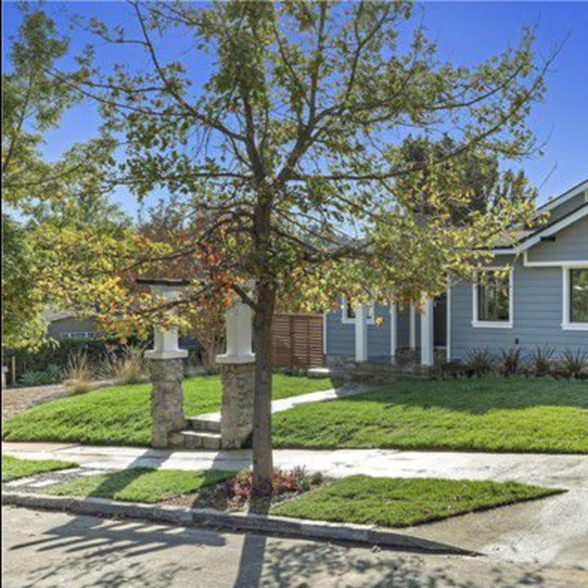 A single-story house with a landscaped front yard features a grey exterior and a wooden fence.