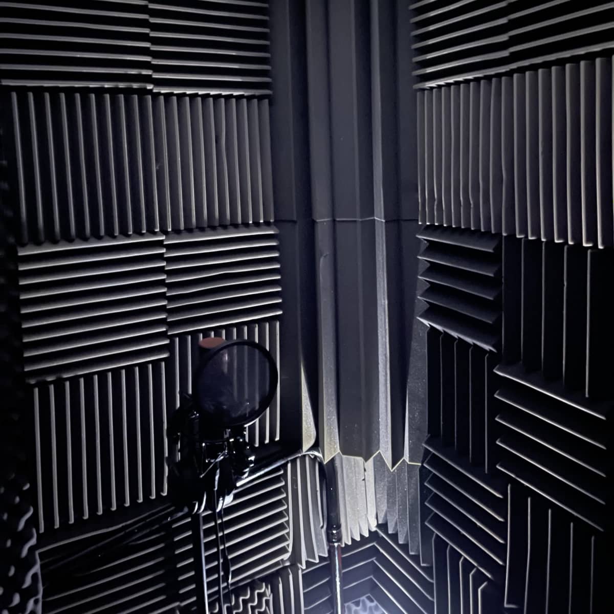 A corner of a soundproof studio, featuring acoustic foam panels and a microphone on a stand.