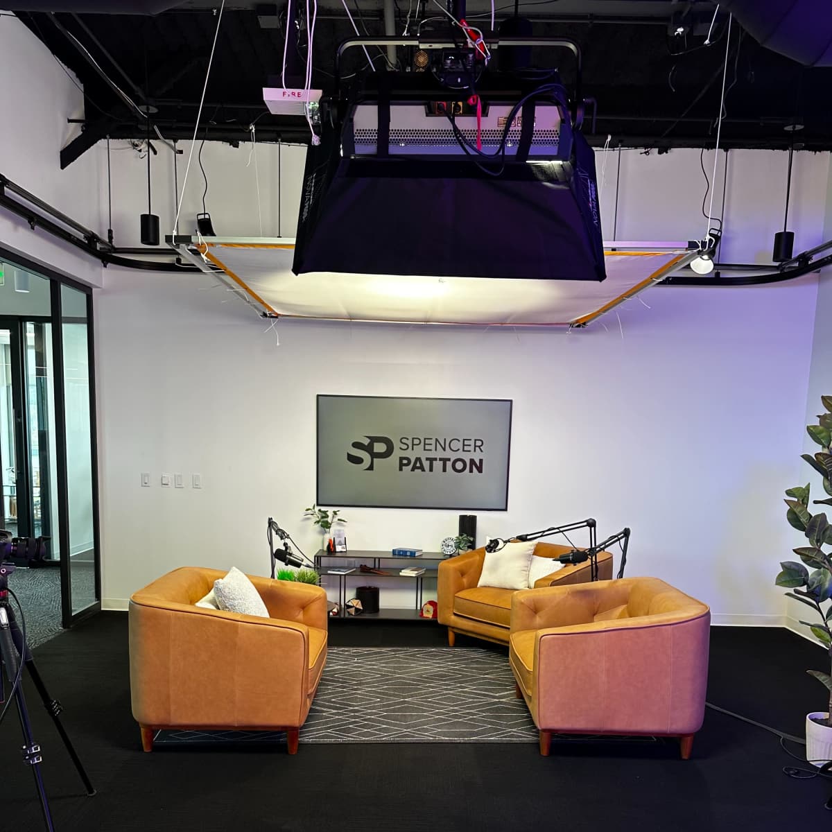 A modern studio setup with two orange couches facing each other, a small table in between, and a sign that reads "SPENCER PATTON" on the wall.