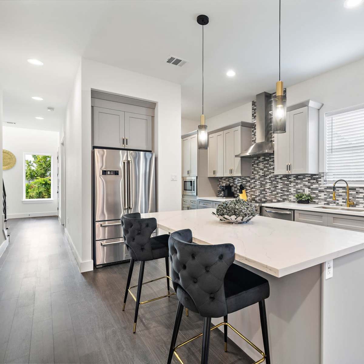 A modern kitchen features sleek cabinetry, stainless steel appliances, and a large island with bar seating, illuminated by pendant lights.